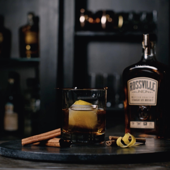 A glass of whiskey and a bottle of Rossville whiskey on a table